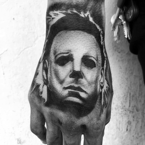 Black and gray Michael Myers hand tattoo, featuring his iconic mask with dark, hollow eyes for a chilling and bold horror design.