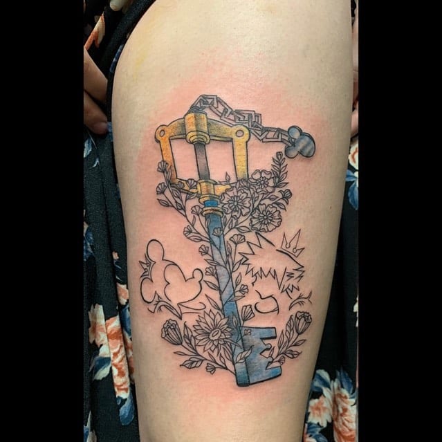 Kingdom Hearts-inspired tattoo featuring a Keyblade with floral elements and Mickey, Sora, and crown silhouettes, blending color and line art.