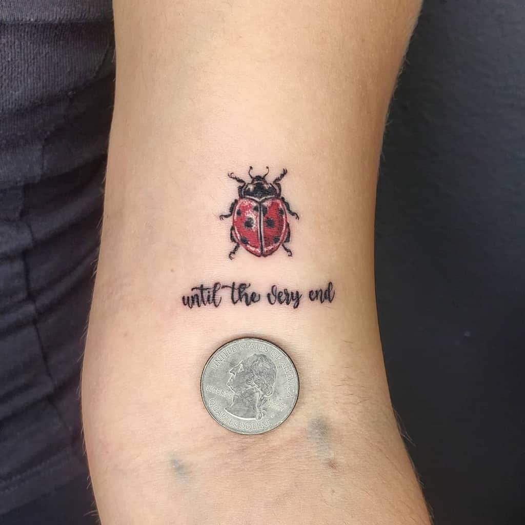 Small, delicate ladybug tattoo with vibrant red details, paired with the phrase 'until the very end,' symbolizing endurance and devotion.