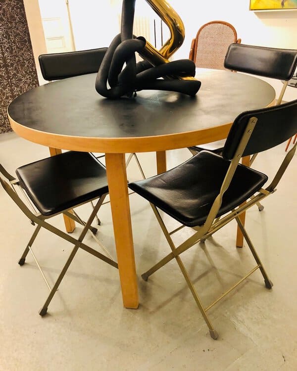 Mid-century modern round dining table with a black top, wooden legs, and folding black chairs.