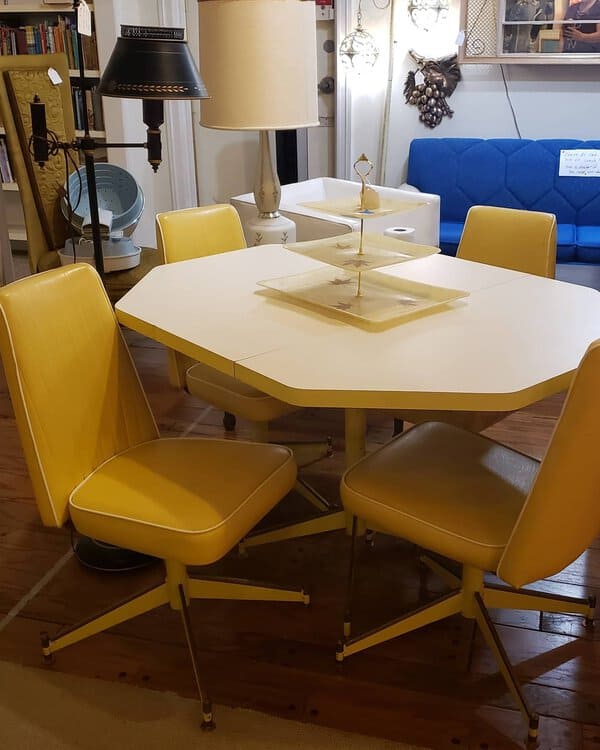 Retro mid-century modern dining set with a white octagonal table and yellow swivel chairs.
