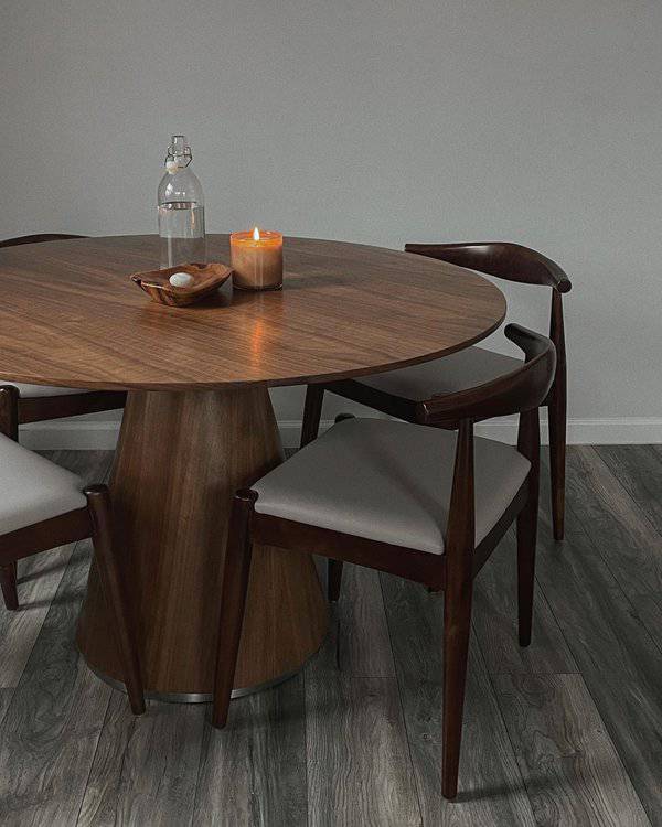 Mid-century modern round wooden dining table with a cone base, dark chairs, and a lit candle.