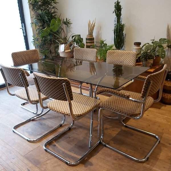 Mid-century modern dining set with a glass table, chrome chairs, and lush indoor plants.