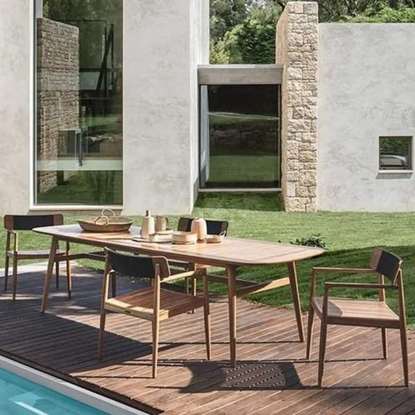 Mid-century modern outdoor wooden dining table with matching chairs on a poolside deck.