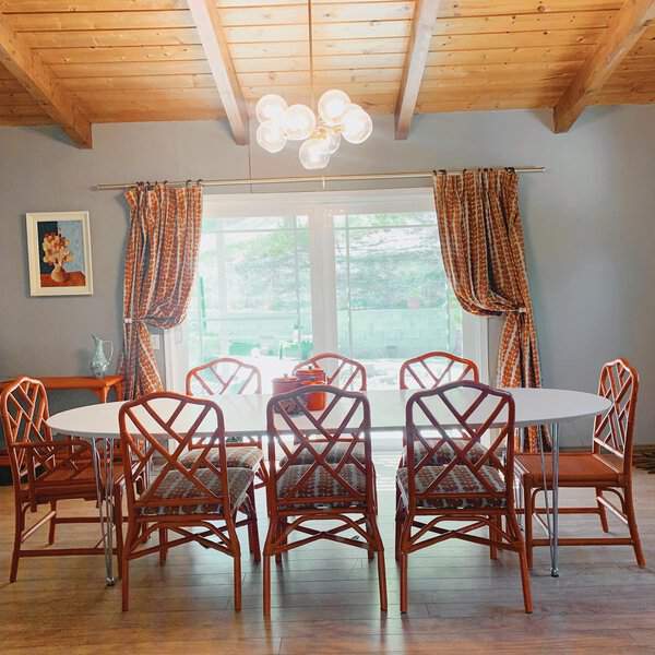 Retro-inspired dining room with an oval table, rattan chairs, and exposed wood beam ceiling.