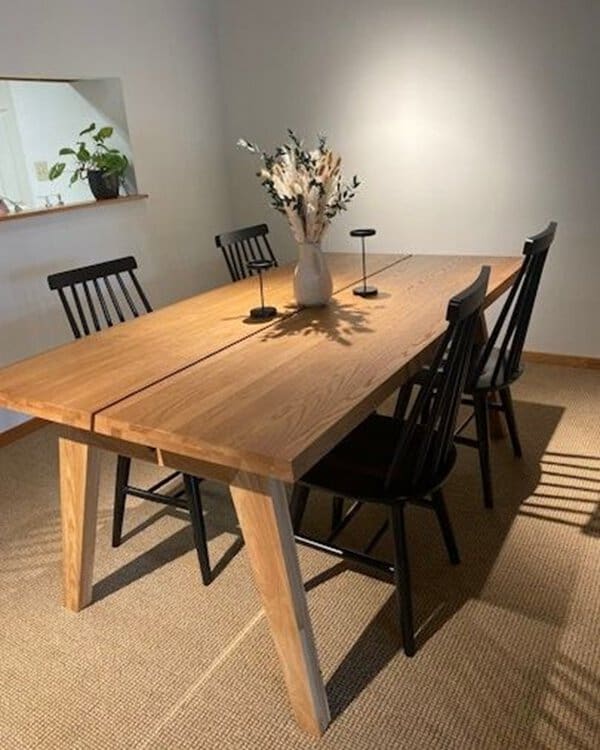 Rustic wooden dining table with black spindle chairs and a minimalist centerpiece in a cozy setting.