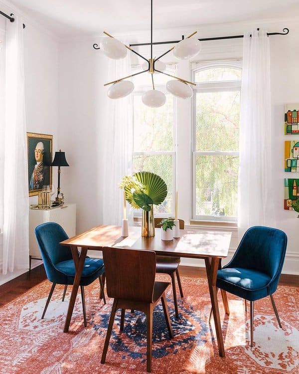 Mid-century modern dining room with a wooden table, velvet chairs, and a statement chandelier.