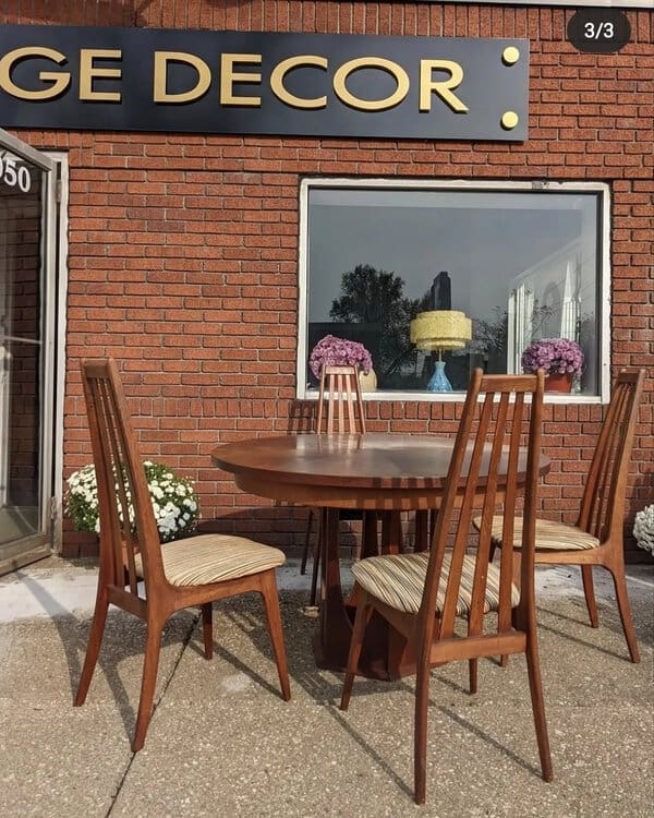 Mid-century modern round dining table with tall-back wooden chairs outside a vintage decor store.