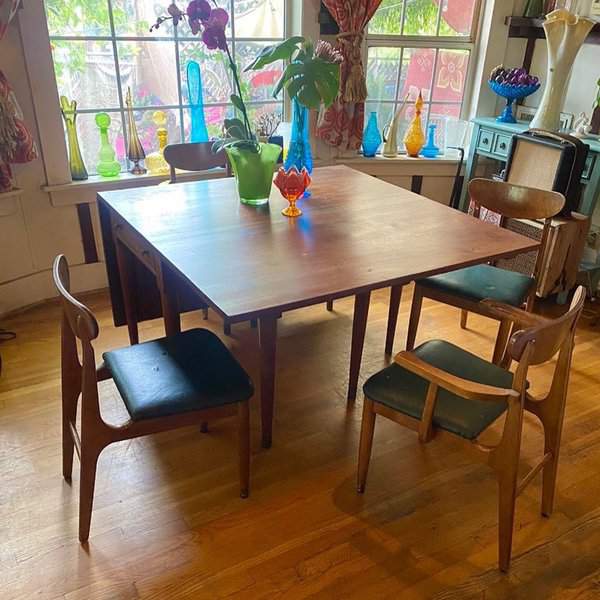 Mid-century modern square dining table with wooden chairs and colorful glass decor by the window.