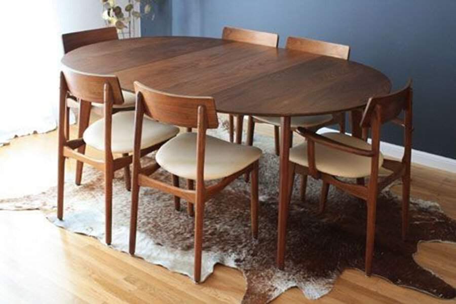 Mid-century modern oval dining table with wooden chairs and a cowhide rug on hardwood flooring.