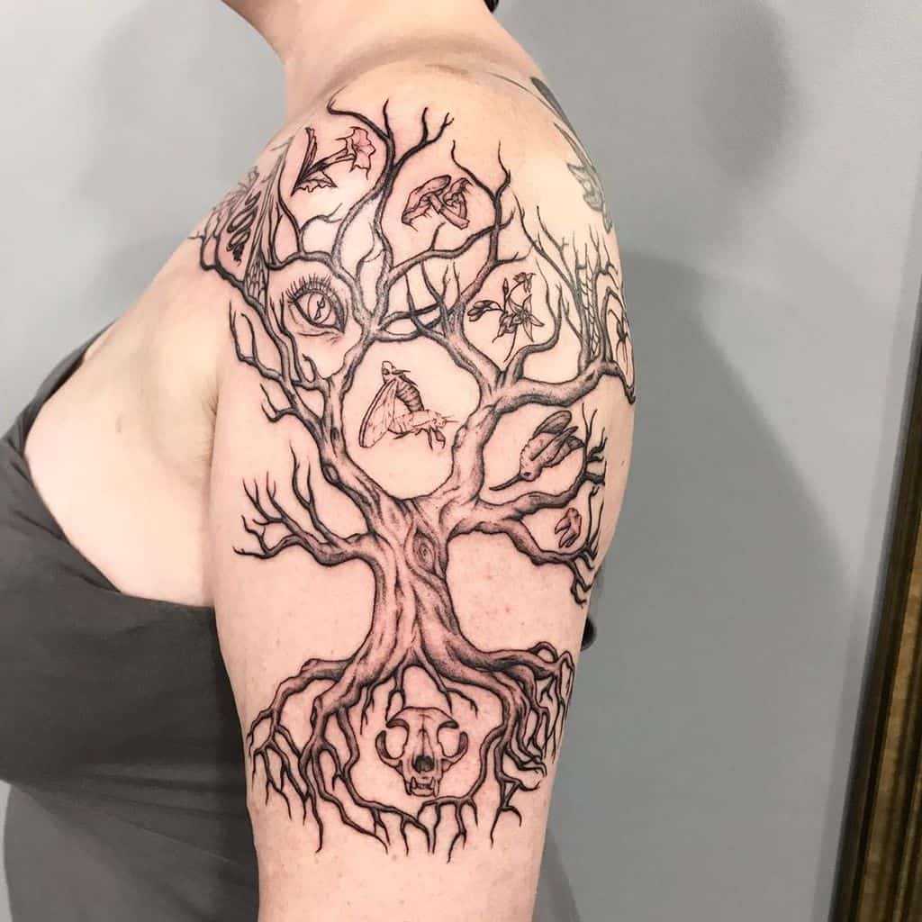 The tattoo features a detailed tree design with various symbols such as eyes, bats, and skulls woven into the branches and roots.