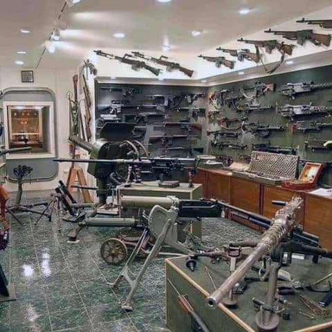 Military-themed firearm room displaying an extensive collection of weapons, from vintage rifles to mounted artillery, with meticulous organization.
