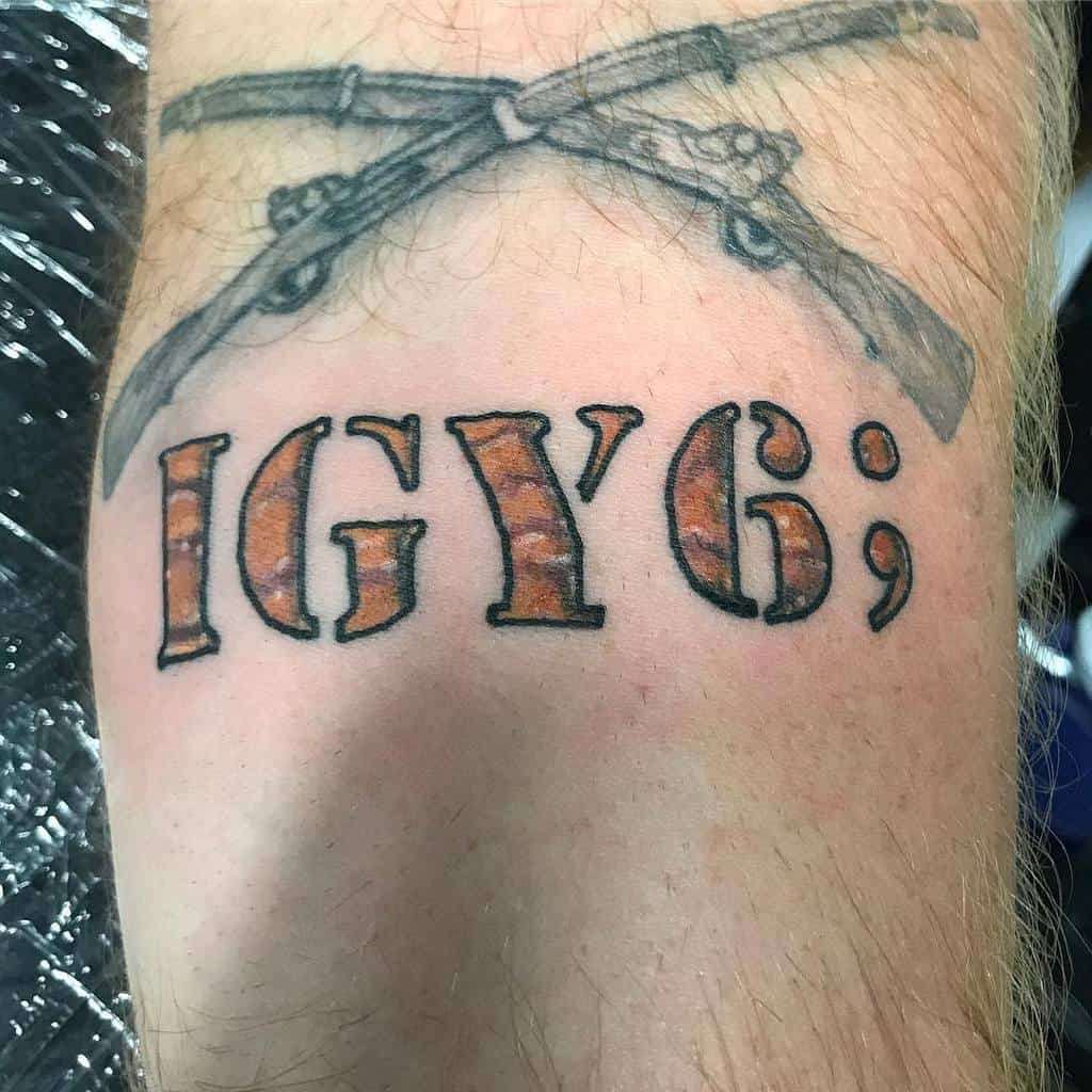 Tattoo of two crossed rifles above the text "IGY6;" on an arm