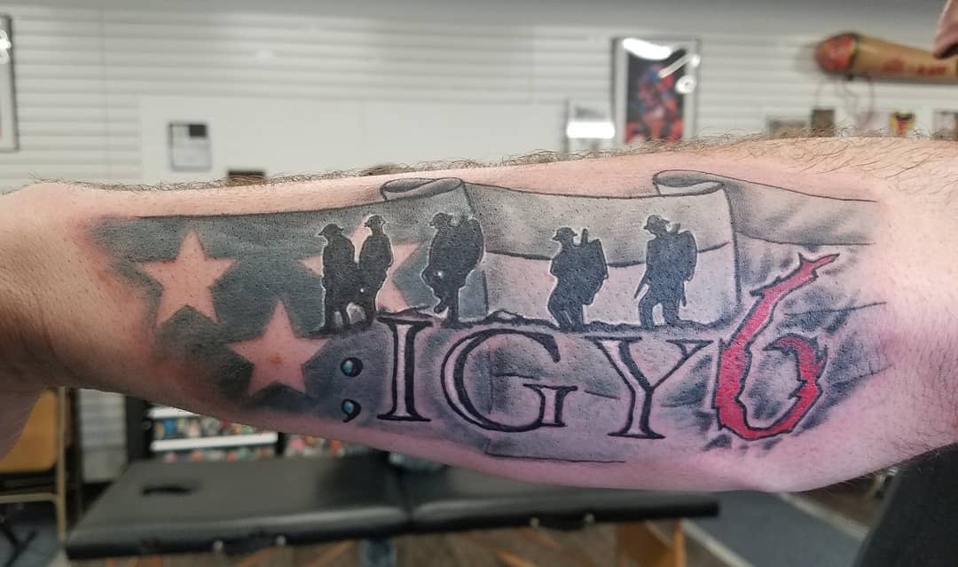 Tattoo featuring soldiers, stars, and ";IGY6" on an arm inside a tattoo studio