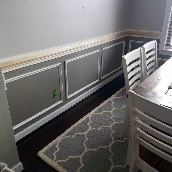 Dining room with white chairs, gray accent wall, a chair rail, and a light gray patterned rug