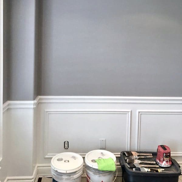 Room with gray walls being painted, paint buckets on the floor, a toolkit nearby, and a chair rail to be installed