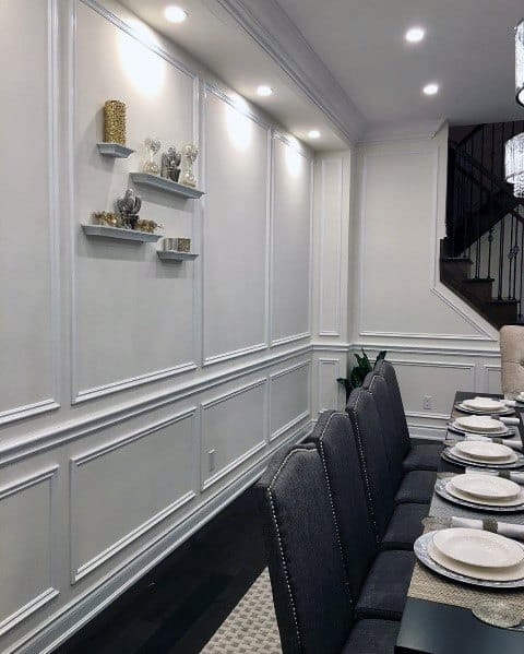 Elegant dining room with a long table, chair rail accents, wall shelves with decorative items, and recessed lighting