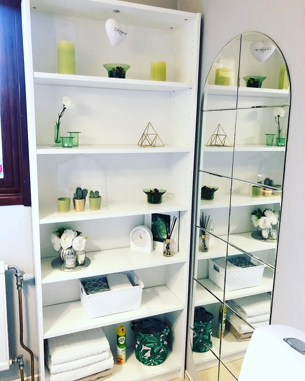 Tall white bathroom shelving unit with decor, plants, and towels next to a large mirror.
