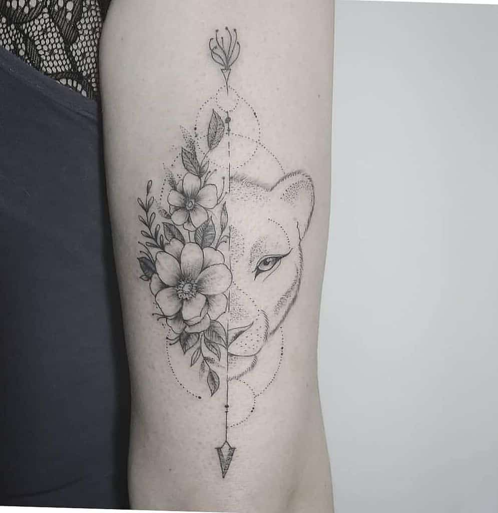 Intricate black and grey lioness tattoo on the arm, featuring half floral details and geometric arrow elements for a delicate yet fierce look.