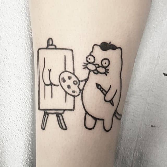 A black ink tattoo of a cartoon cat artist with a mustache and beret painting a butt on a canvas, blending humor with a playful style.