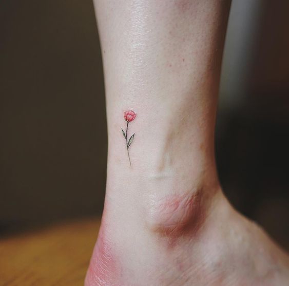 A tiny red tulip tattoo on the ankle, featuring a delicate flower with a thin green stem and small leaves in a minimalist design.