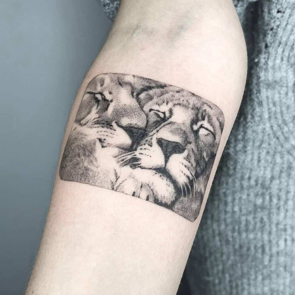Tattoo of two lions' faces close together on an arm with a gray background beautifully detailed with single needle precision