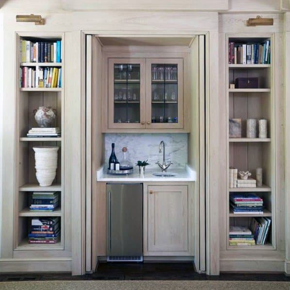 Elegant mini wet bar integrated into light wood built-in bookcases, creating a sophisticated and functional design