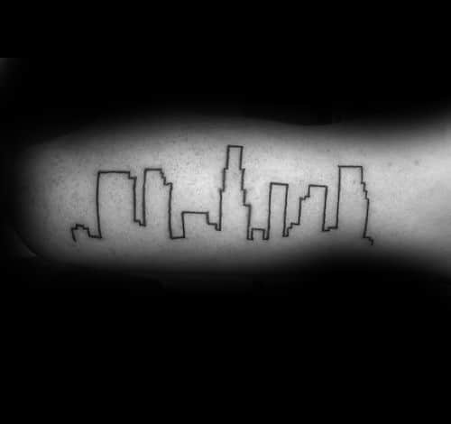 Minimalist tattoo of the Los Angeles skyline outlined in thin black ink across the inner arm.