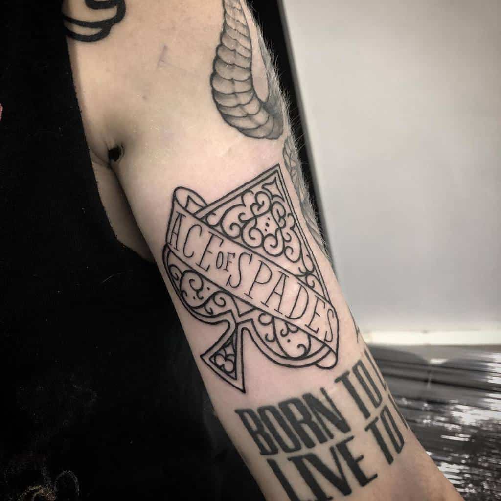 A black-and-white tattoo of the Ace of Spades symbol, with ornate detailing and the words "Ace of Spades" inside, accompanied by the phrase "BORN TO LIVE TO" below