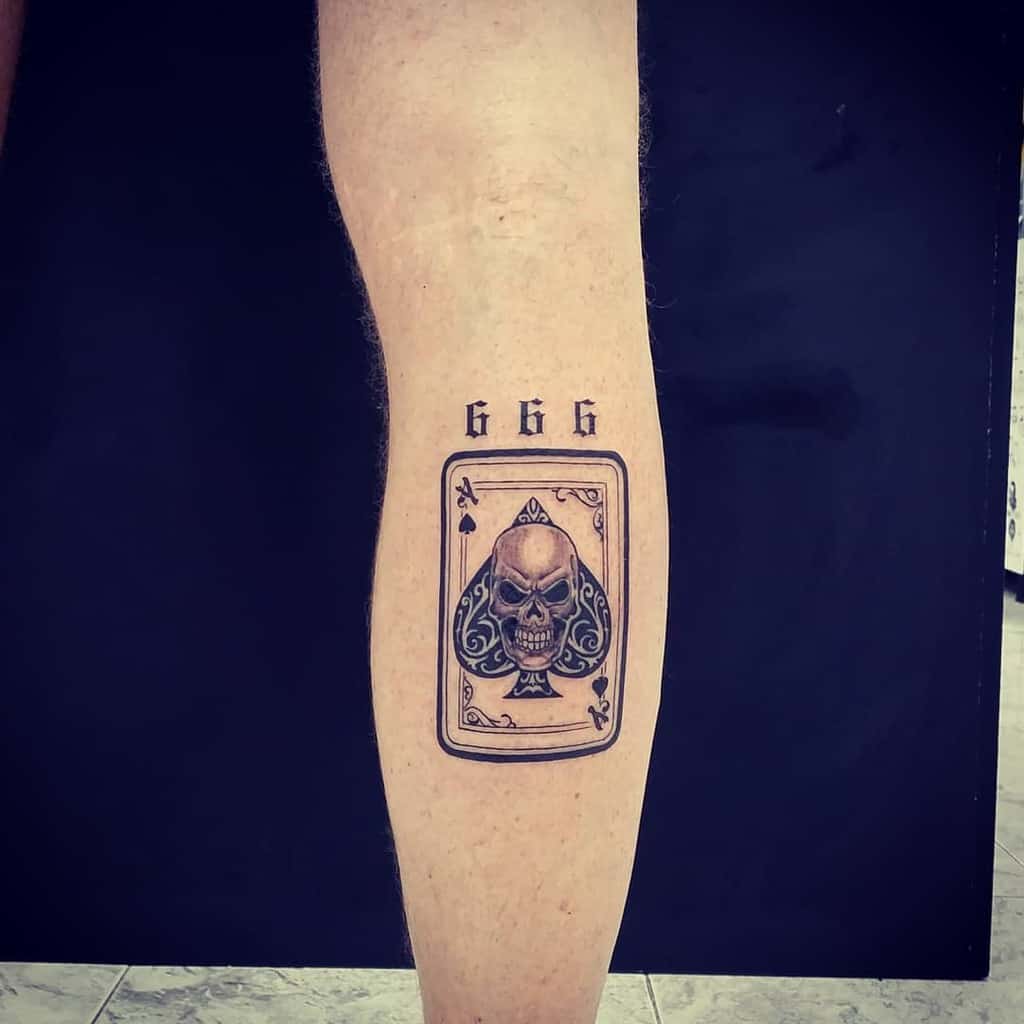 A black-and-white tattoo featuring the Ace of Spades card with a skull in the center, and the number "666" written above it