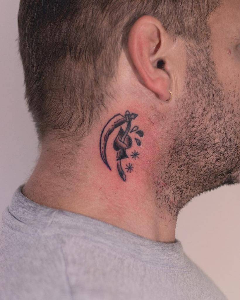 A black-and-white tattoo of a spade stab by a scythe, with small asterisks and droplets surrounding the design