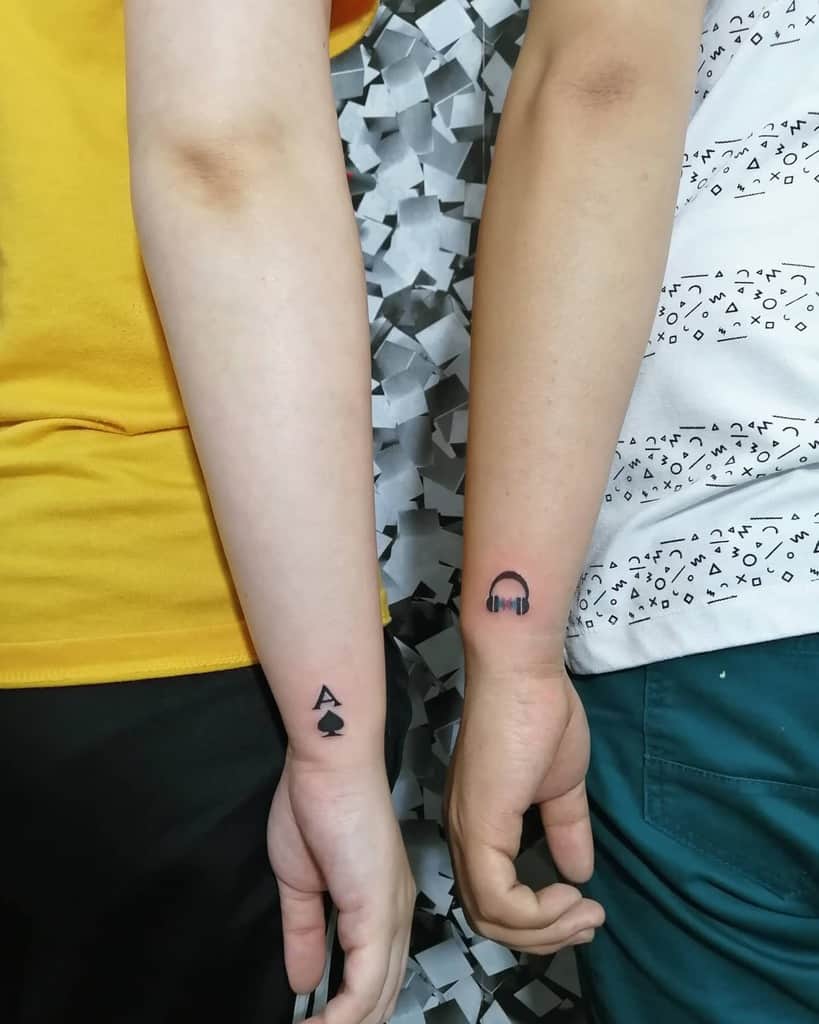 A tattoo of the Ace of Spades symbol on one arm and a pair of headphones on the other