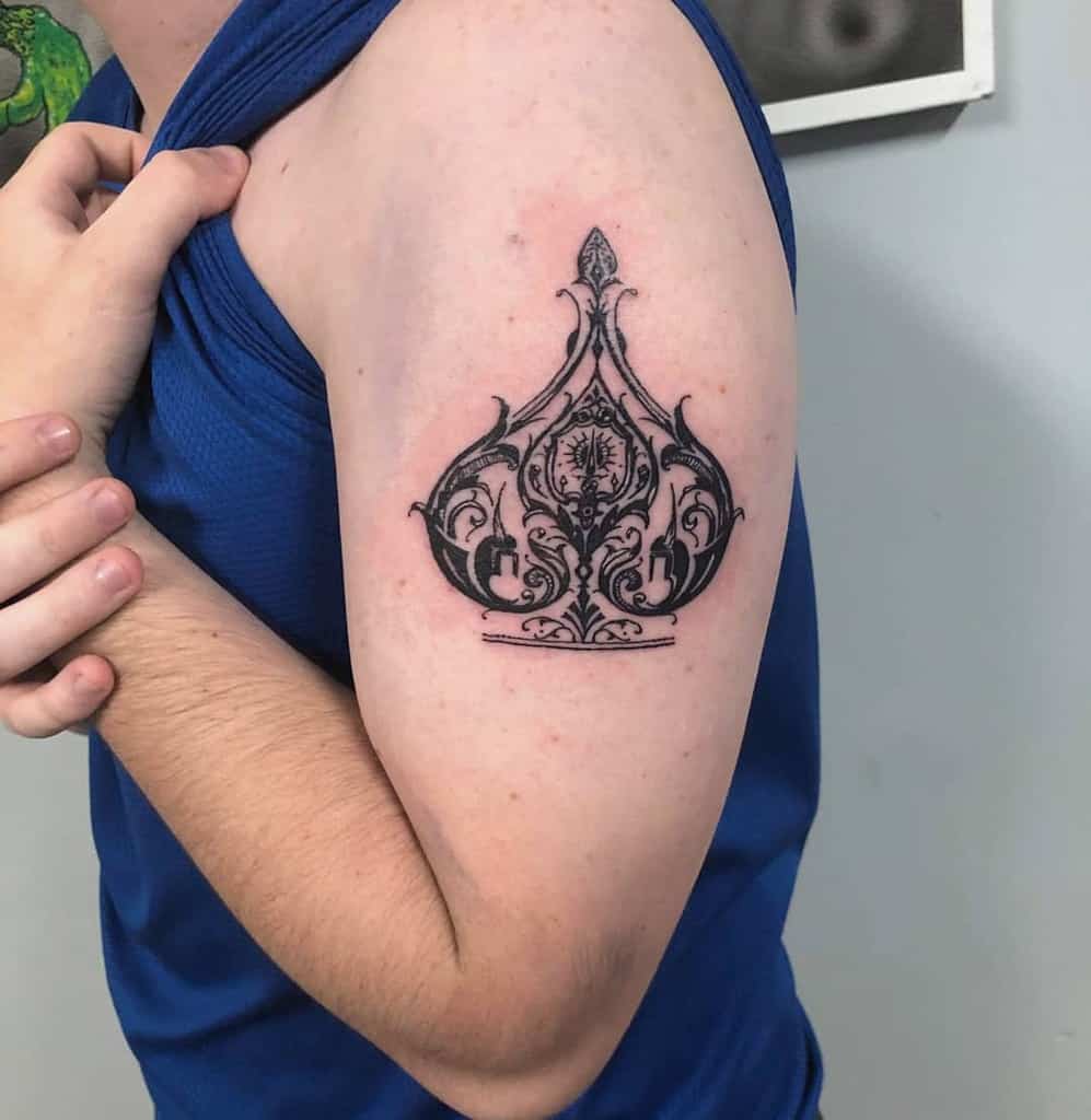 A black-and-white tattoo of the Ace of Spades symbol, designed with intricate ornamental detailing