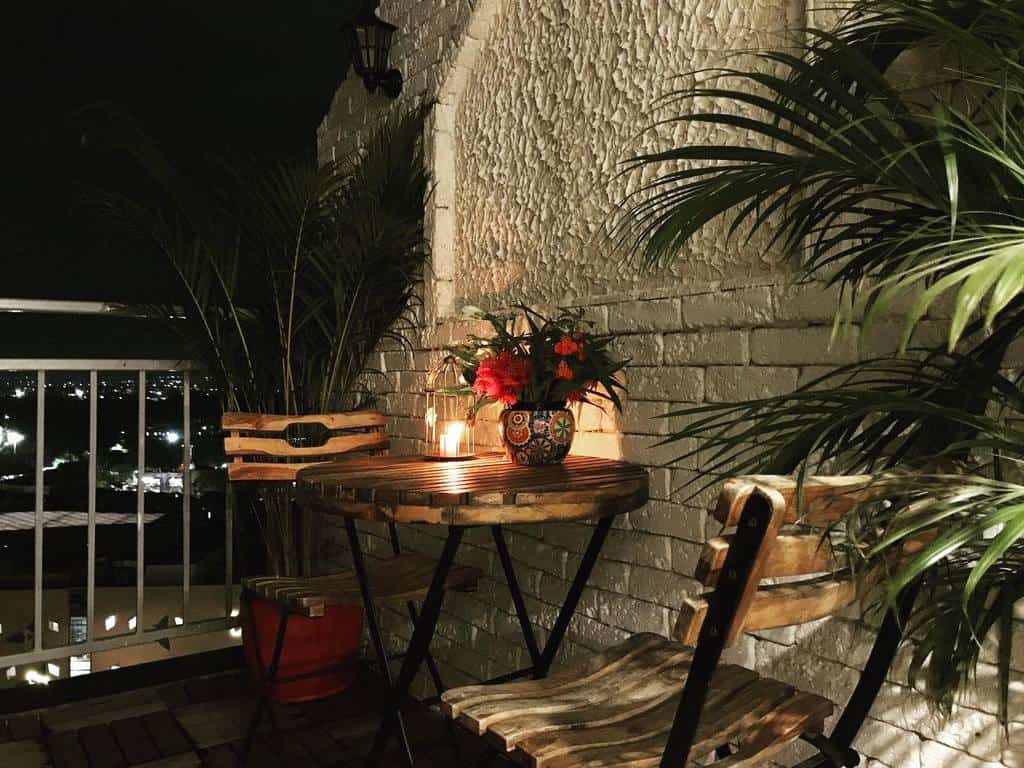Cozy nighttime balcony with wooden table and chairs, potted plants, and candlelight ambiance.