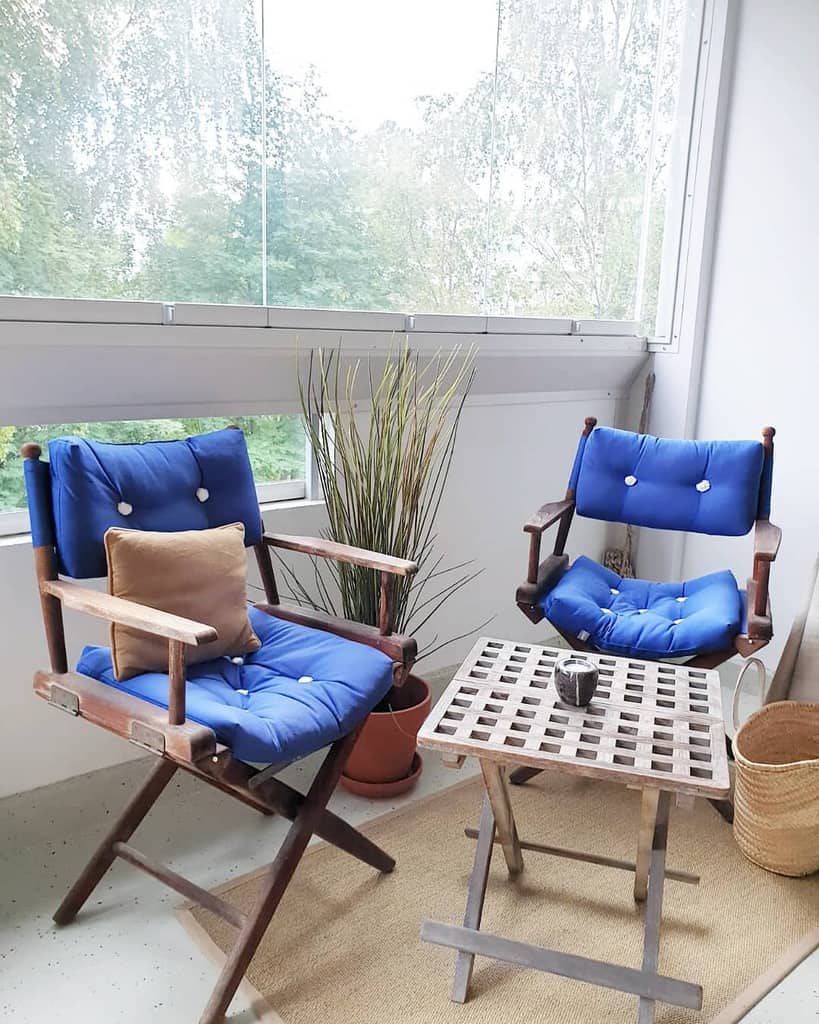 Minimalist balcony with wooden chairs, blue cushions, small table, and a potted plant.