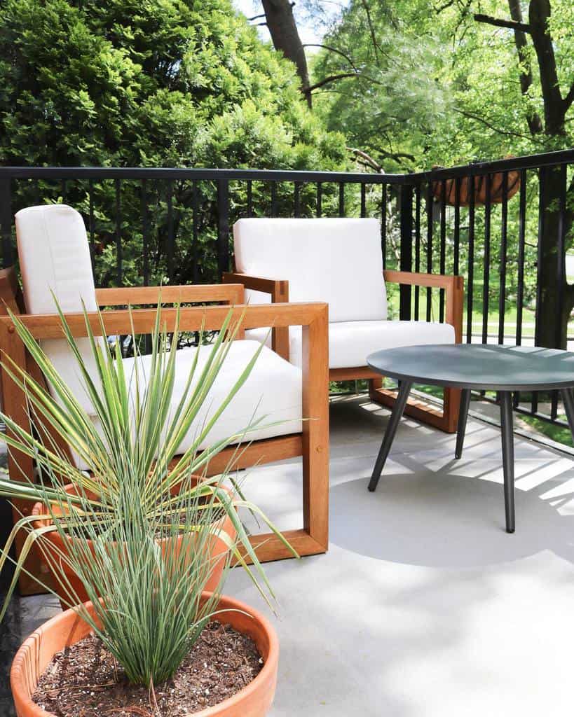 Minimalist balcony with wooden chairs, white cushions, a small round table, and potted plants.