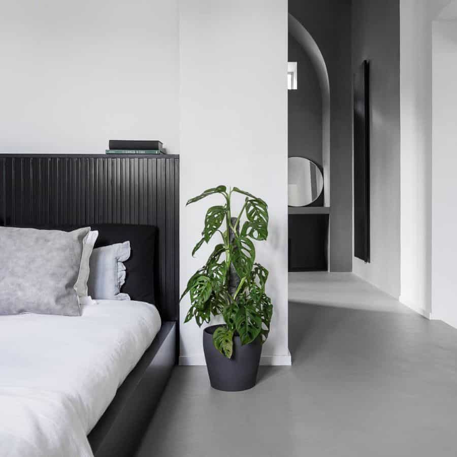 Minimalist bedroom with black headboard, white bedding, and potted monstera plant.