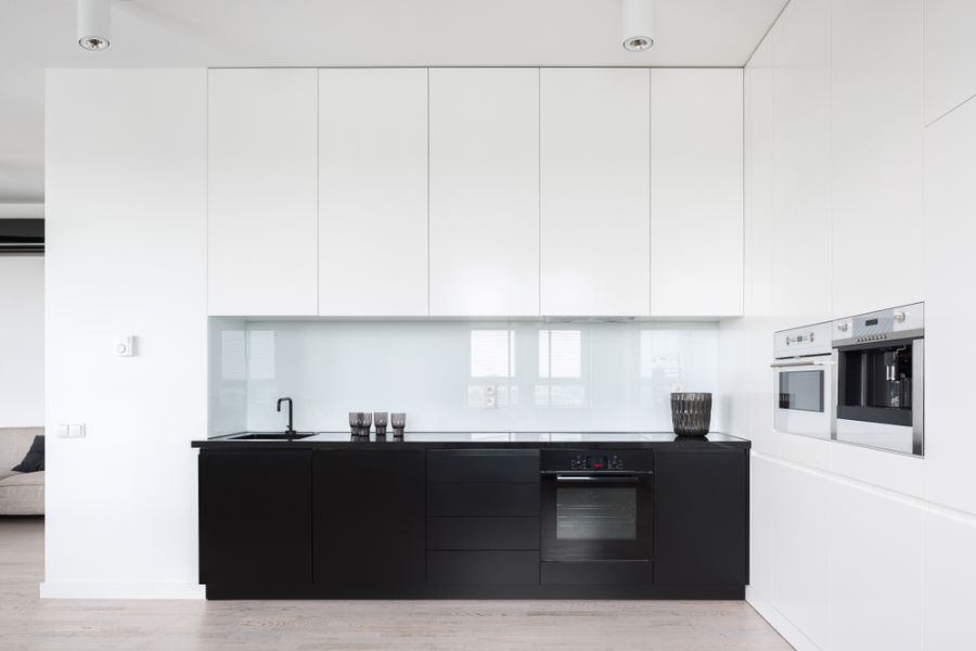 Minimalist kitchen with black lower cabinets, white upper cabinets, and a glass backsplash.