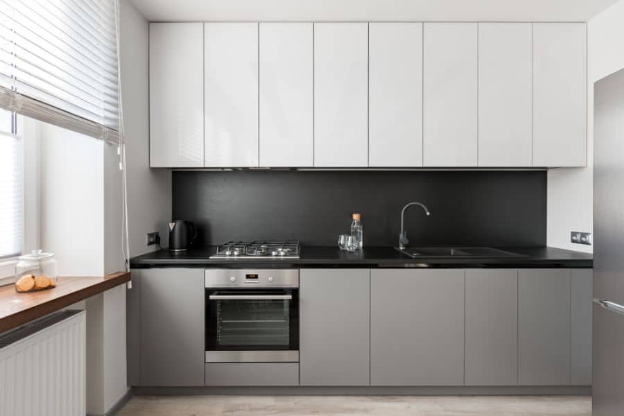 Modern kitchen with white upper cabinets, grey lower cabinets, and black countertops.