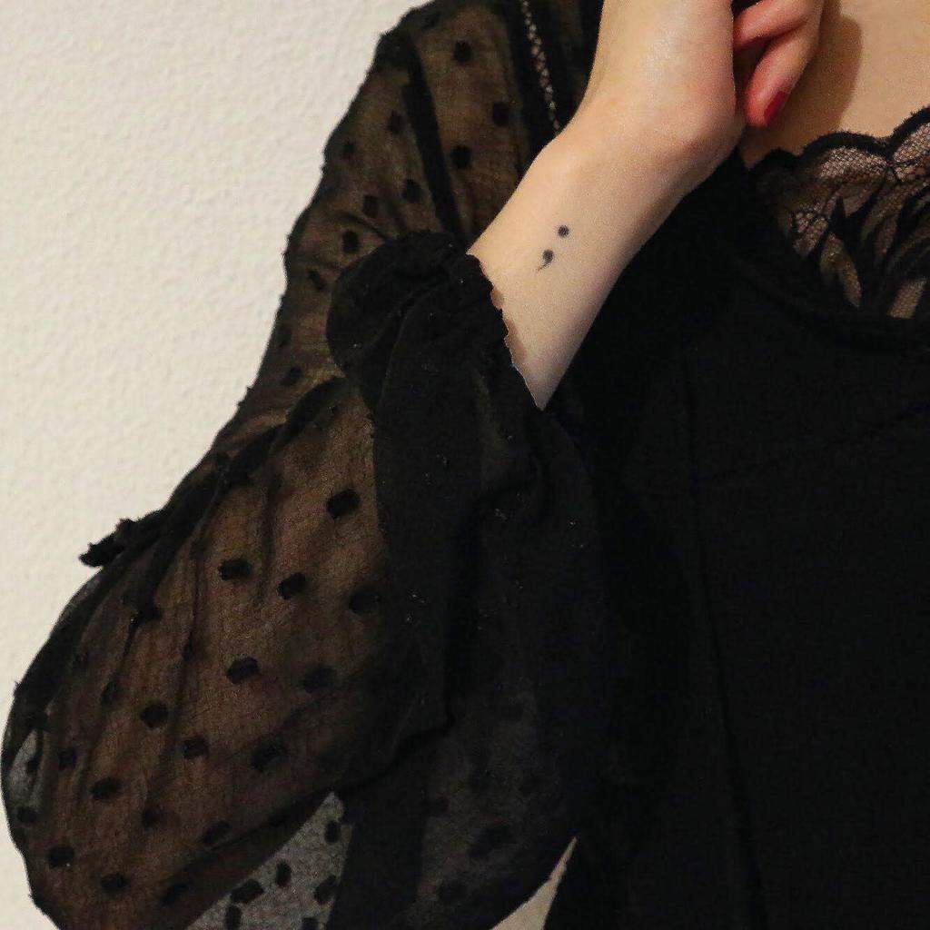This image shows a semicolon tattoo on a person's wrist, symbolizing resilience and hope.
