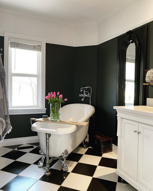 Farmhouse bathroom with black walls, clawfoot tub, checkered floor tiles, and pink flowers.