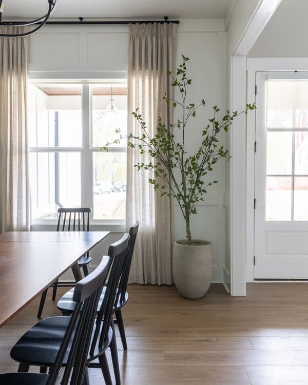 Minimalist dining room with neutral linen curtains, black chairs, and a modern potted plant.