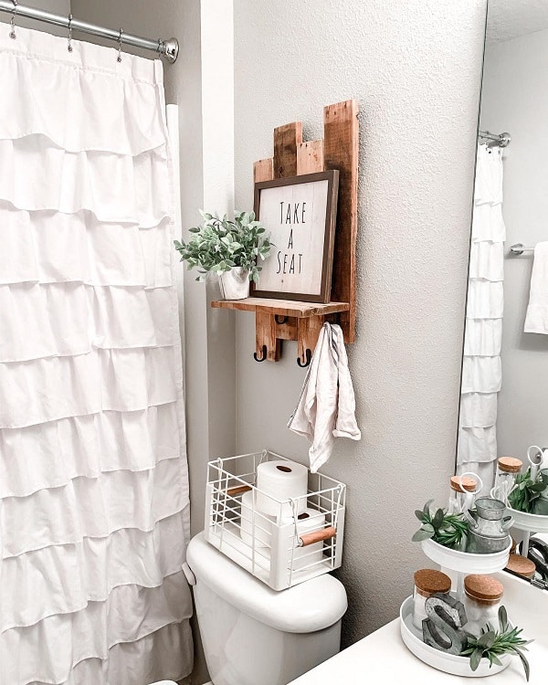 Farmhouse-style bathroom with a plant, white shower curtain, and "Take a Seat" sign above the toilet
