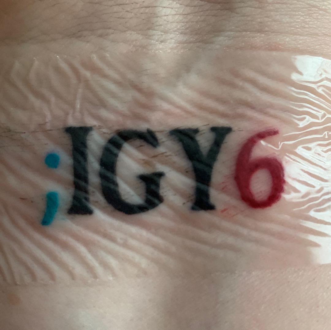 Close-up of a tattoo reading ";IGY6" in black, with the semicolon in blue and the number six in red