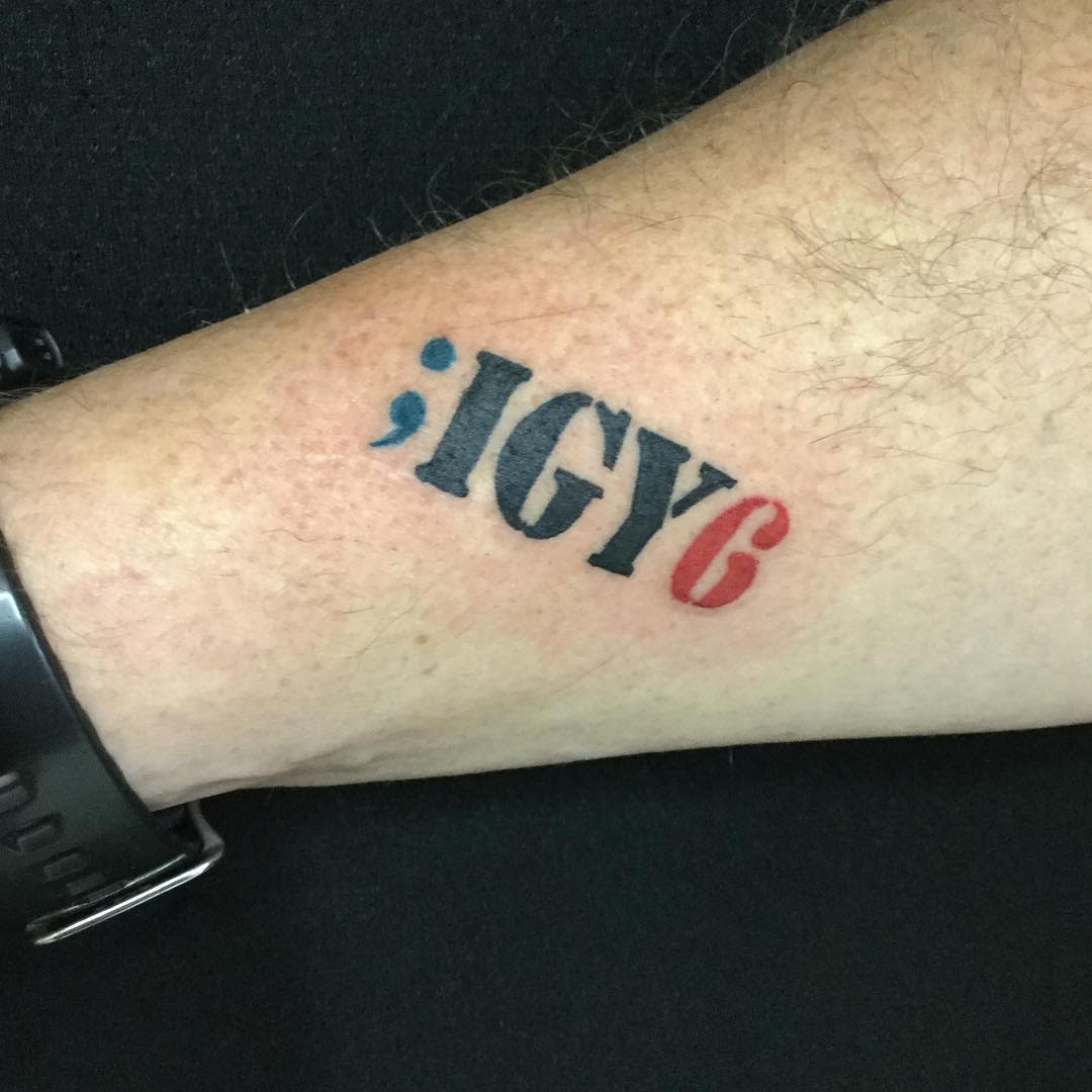 Minimalist ';IGY6' tattoo in black, blue, and red ink on the wrist, symbolizing support and awareness for mental health