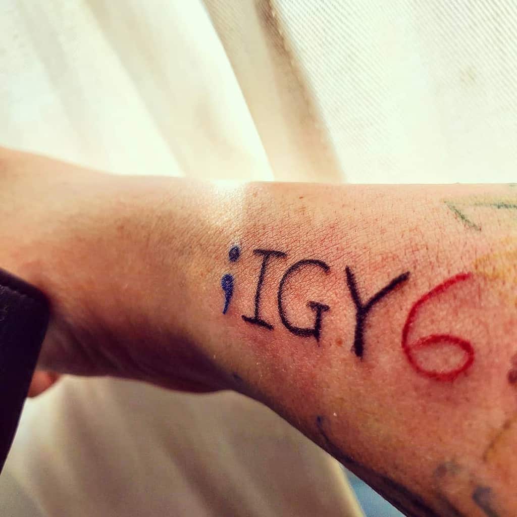 Forearm tattoo of ";IGY6" with the "6" in red, symbolizing support for mental health awareness and solidarity