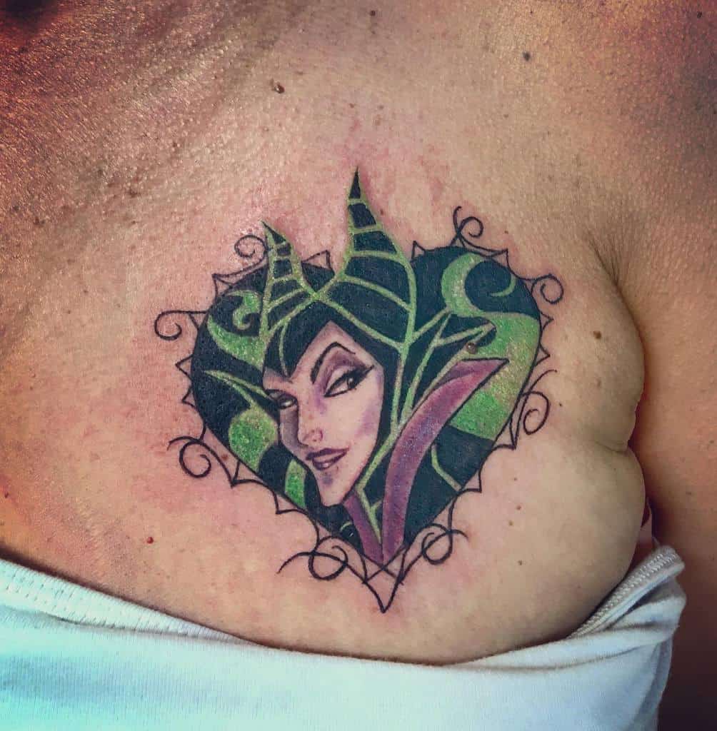 Heart-shaped tattoo of a horned Maleficent character with a green and purple design on a chest