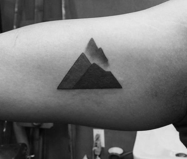 Minimalist geometric mountain tattoo on the arm, featuring bold black triangles with soft shading for a modern and abstract nature-inspired design.