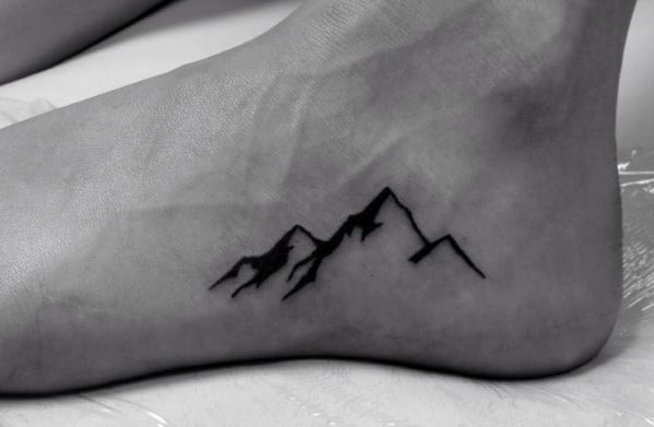 Minimalist mountain tattoo on the foot, featuring bold black peaks with simple lines for a sleek and nature-inspired design.