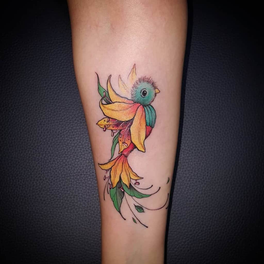 A colorful tattoo of a stylized bird with yellow and green feathers, incorporating floral elements, on an arm